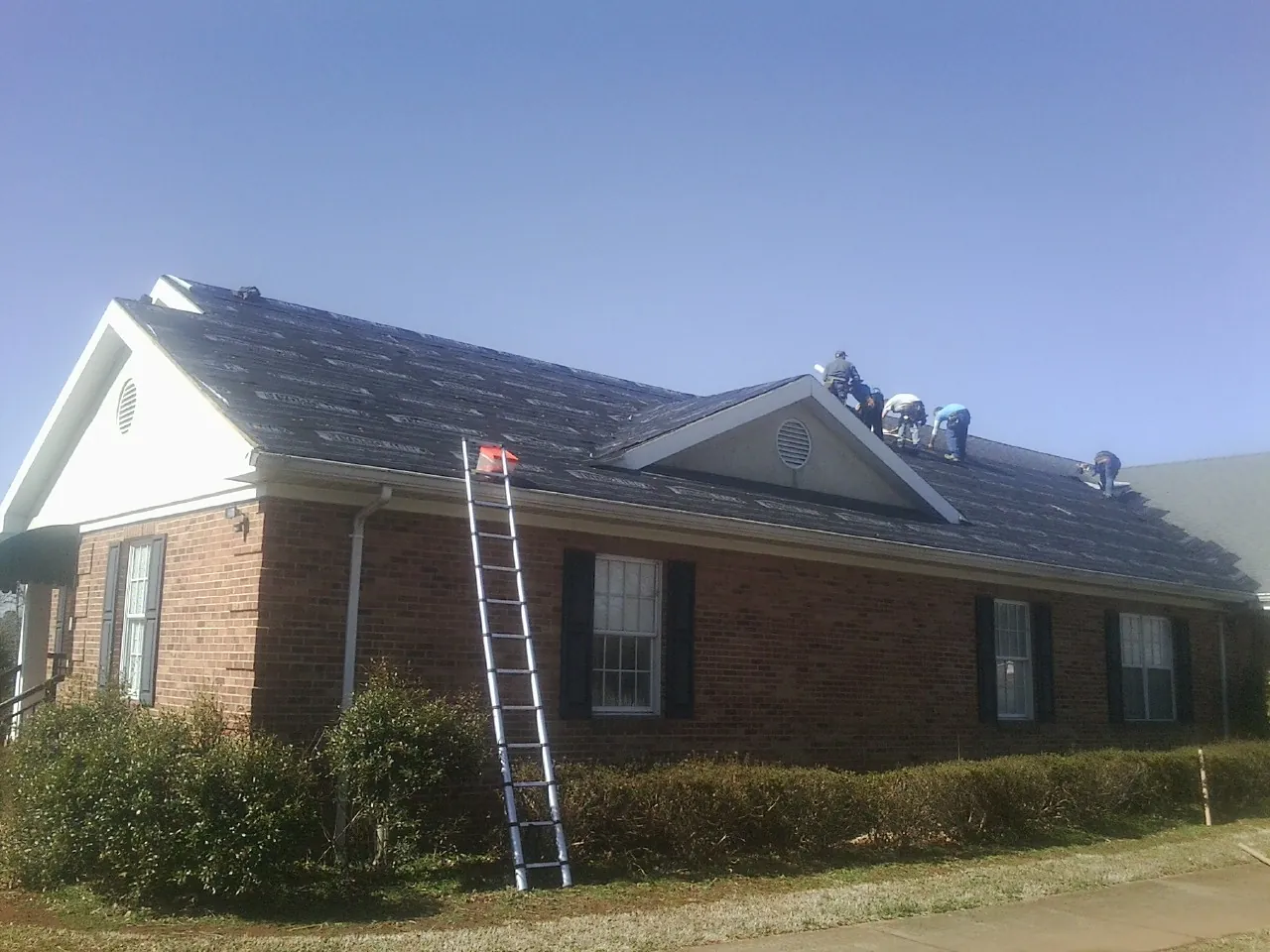 Crew tearing shingles off a brick ranch roof with a ladder set — Metal Roof Repair work by our crew in Leetsdale