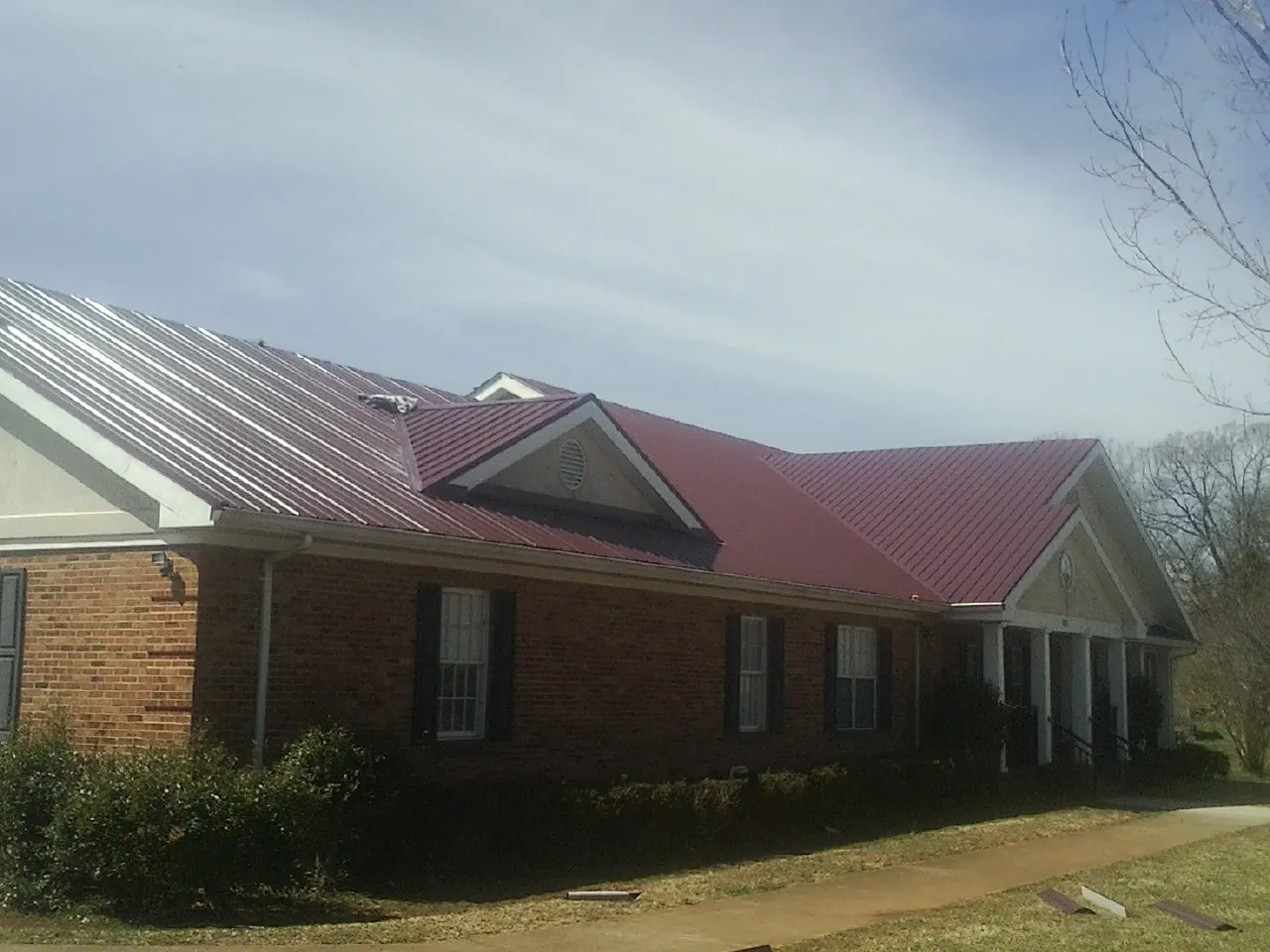 Red metal roof with gabled entries on a long brick building, from a Hail Damage Roof Repair job in Leetsdale