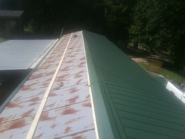 Old rusted panels beside newly installed green metal roofing — Wind Damage Roof Repair by Roofing Brothers in Leetsdale