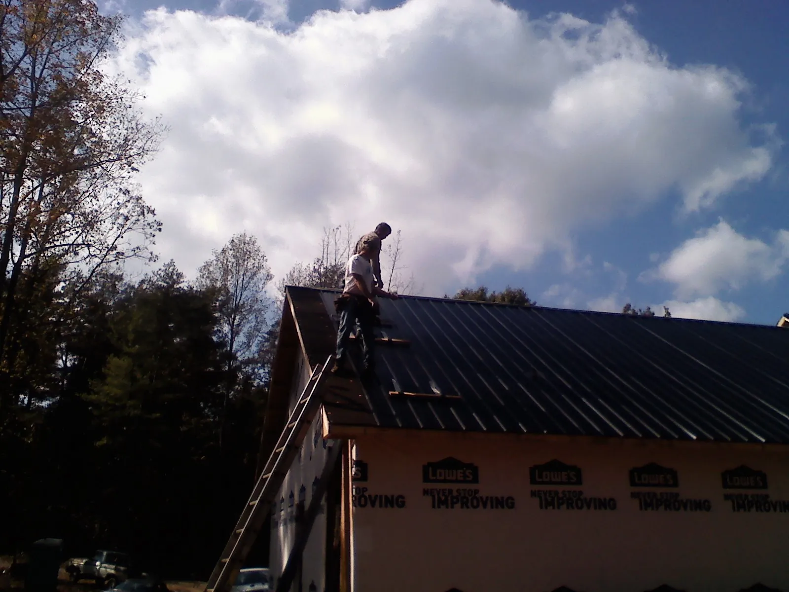 Roofer fastening dark metal panels high against a cloudy sky, from a Roof Inspection job in Leetsdale