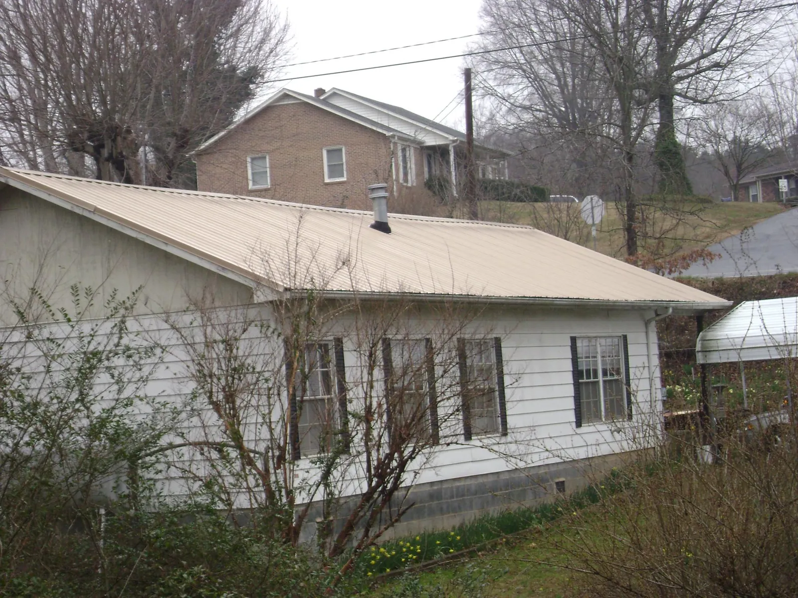 Tan metal roof on a white sided house set into a hillside — Commercial Roofing by Roofing Brothers in Leetsdale
